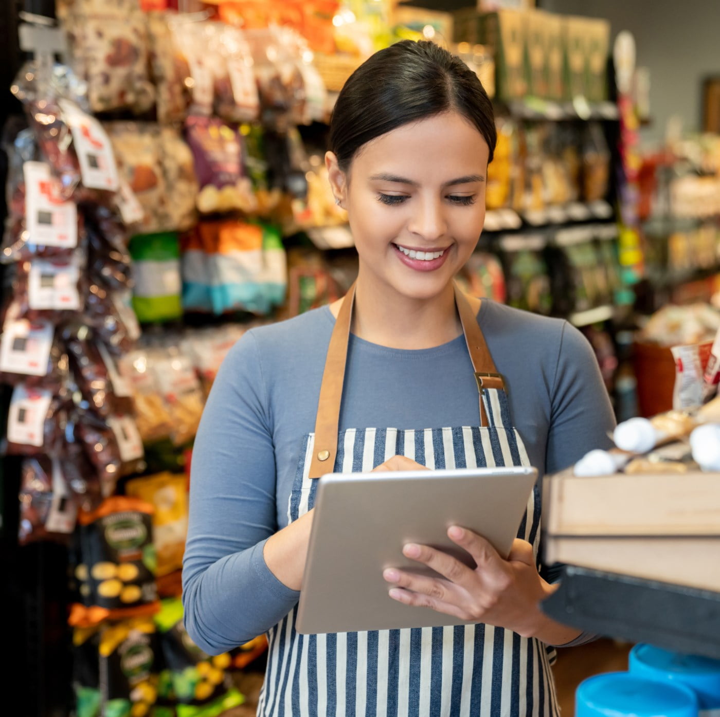 Smilende butikkmedarbeider i et stripete forkle bruker et nettbrett i en butikk.